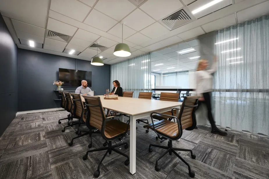A contemporary meeting room featuring a long wooden table surrounded by leather chairs