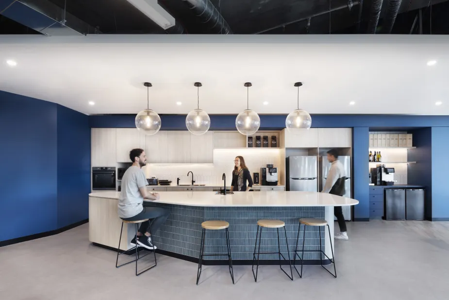 A modern office kitchen with a curved island, Hugo bar stools, white subway tile backsplash, and large globe pendant lights.