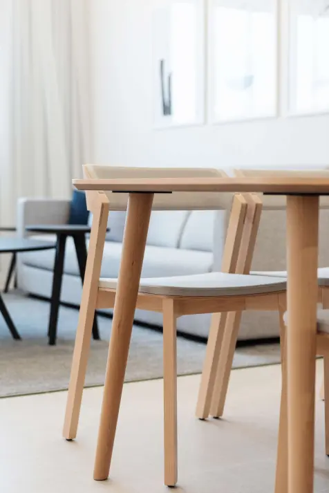 Detail shot of a light wooden dining table and chairs with beige cushions in a bright living area