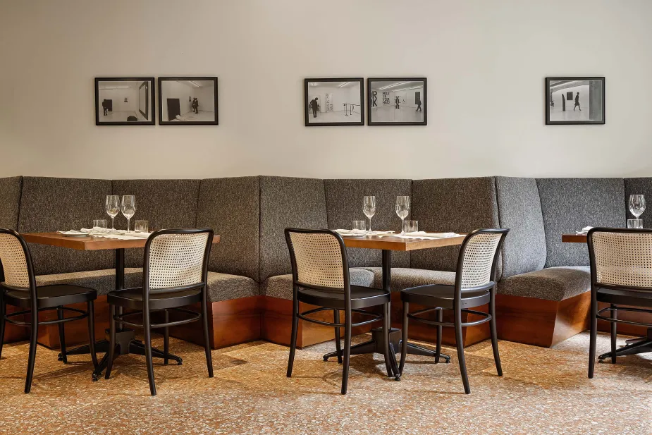 Elegant dining setup featuring a long, textured gray sofa with wooden tables set in front, each adorned with wine glasses and cutlery.