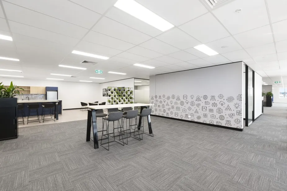 A view of an office area with a high table and stools, near a wall with a creative doodle design.