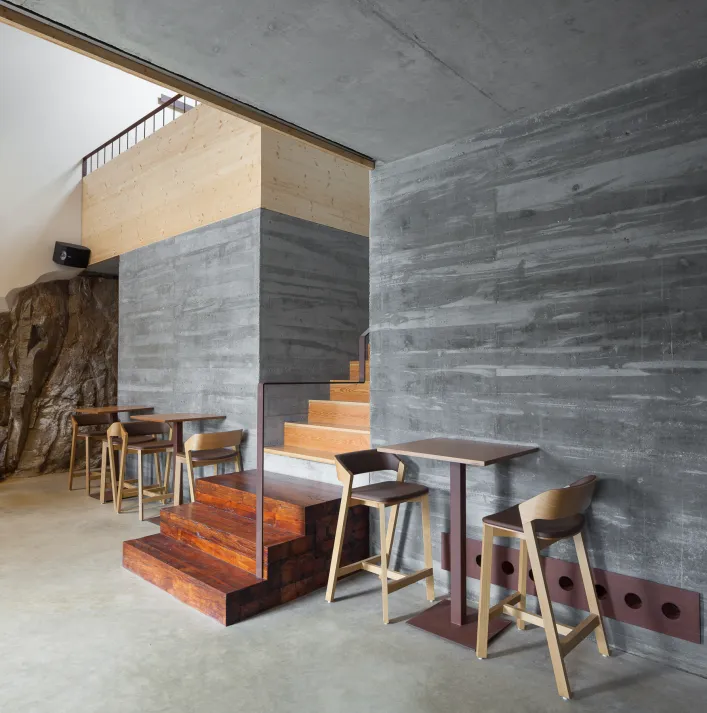 Wooden tables and Merano stools next to a grey wall