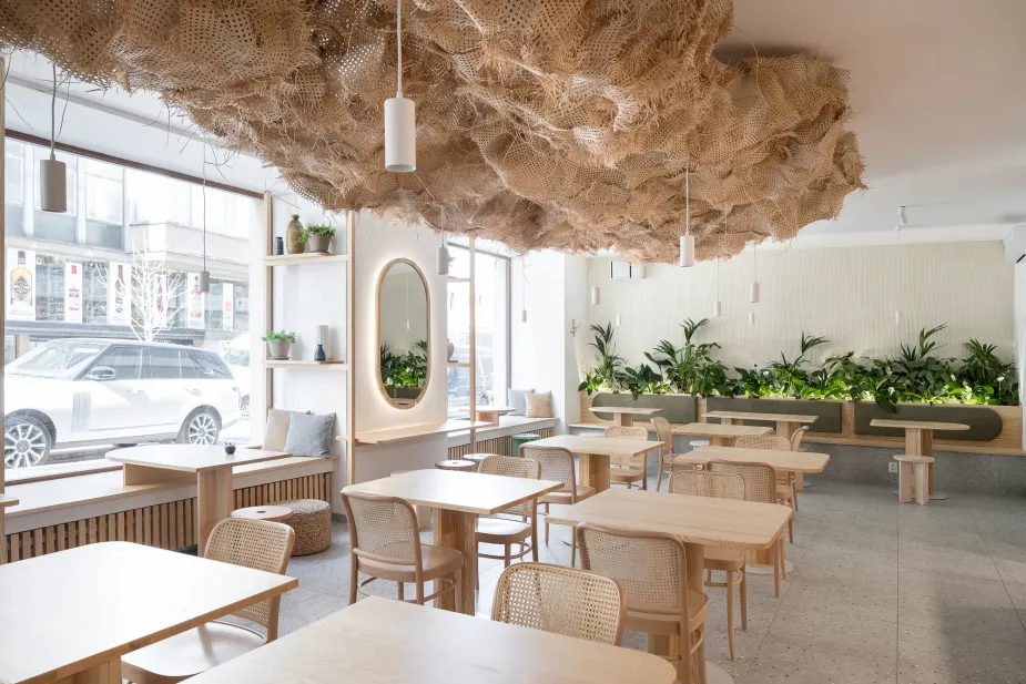 Bright and airy bistro interior with a large organic-shaped rattan cloud hanging from the ceiling, illuminated by pendant lights. 