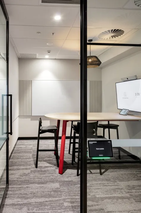 A modern meeting room featuring a wooden round table surrounded by black Andi stools 