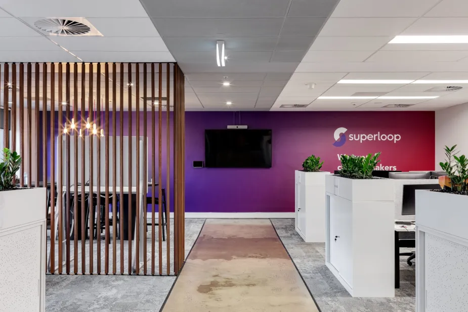 A modern office interior with vibrant design elements, including a purple feature wall with the Superloop logo and wooden slats creating a semi-partition