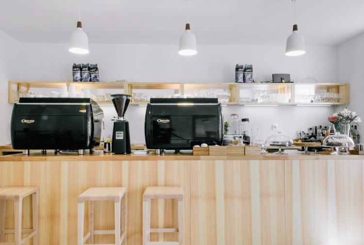 The café counter features sleek black espresso machines flanked by coffee accessories and a coffee grinder