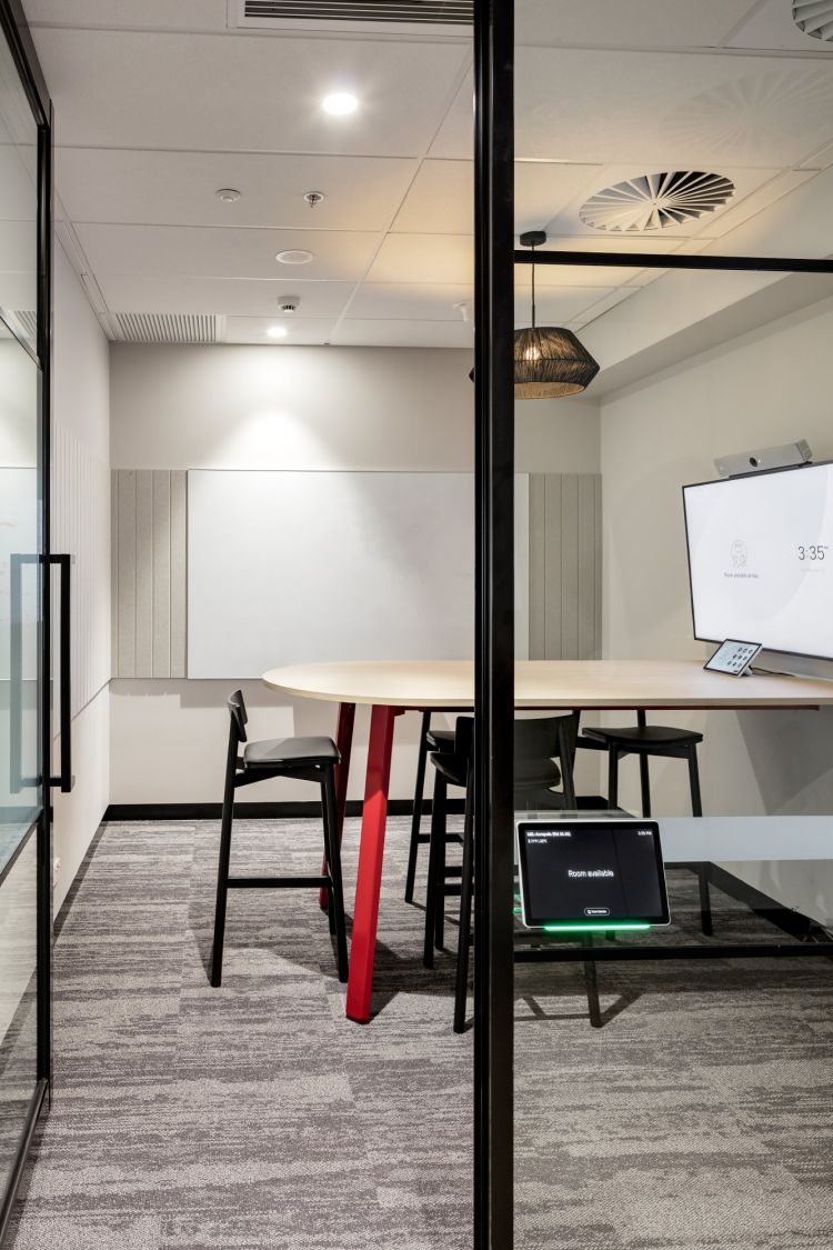 A modern meeting room featuring a wooden round table surrounded by black Andi stools