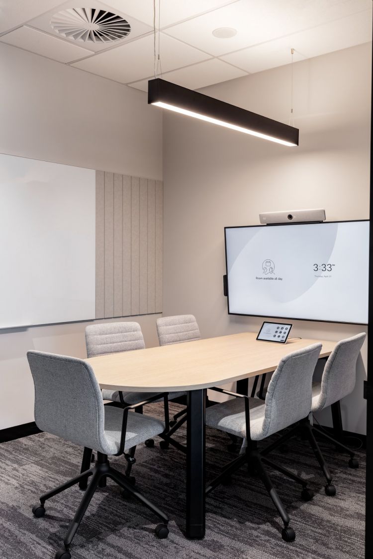 A contemporary meeting room with a rectangular wooden table surrounded by grey upholstered chairs.