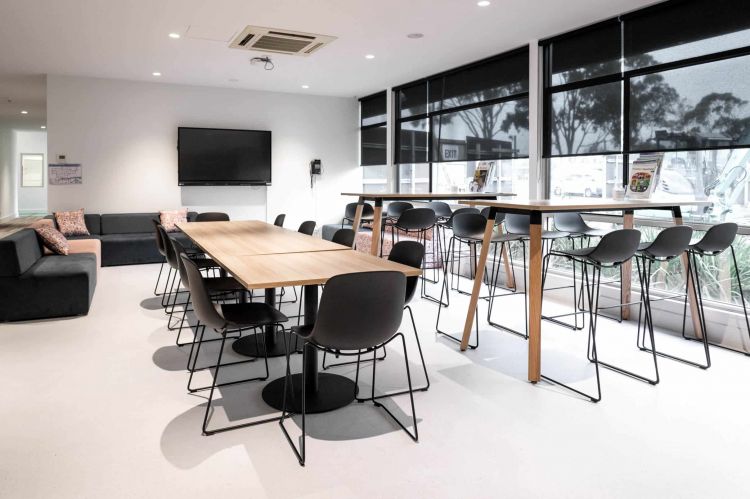 A spacious room with large windows letting in natural light, furnished with a long wooden table and black chairs in the center