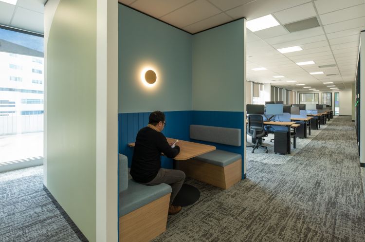 An office breakout area featuring a booth-style seating with a staff sitting at a wooden table, focused on reading or writing.