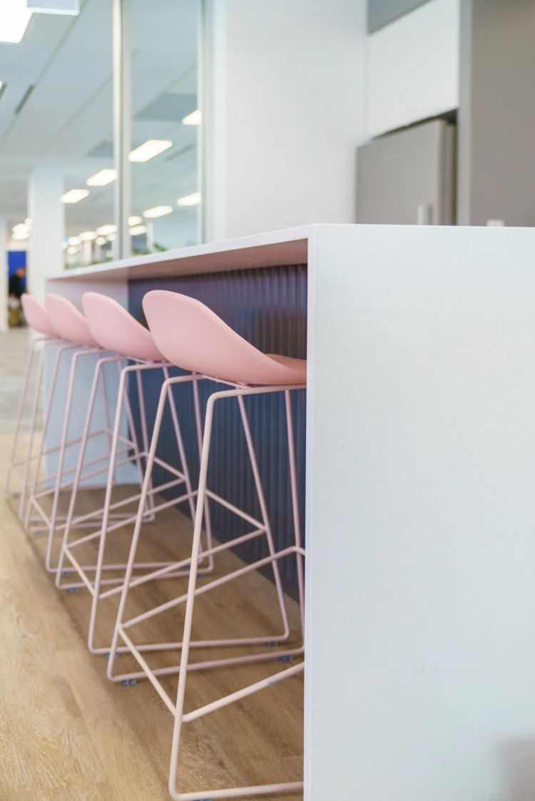Side view of a white counter with pink chairs and metallic legs in an office setting