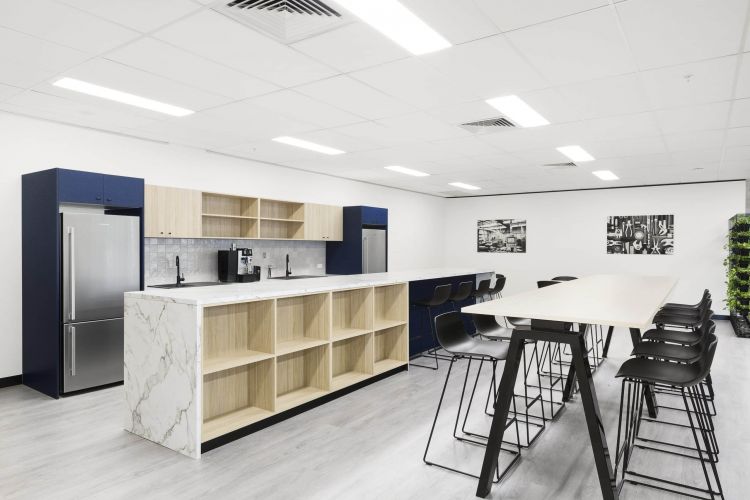 An office kitchenette with light wood cabinets, a marble island, and black stools